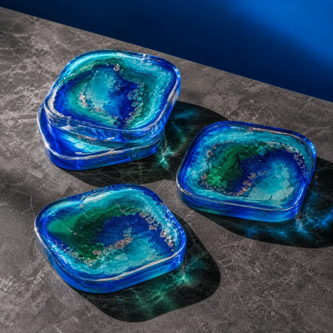 Vier quadratische Epoxidharz-Untersetzer mit intensiven blau-grünen Schichten